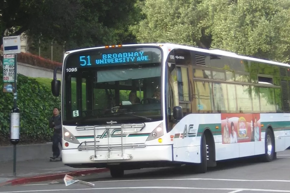 White bus pulling up to sidewalk bus station in Berkeley, California.